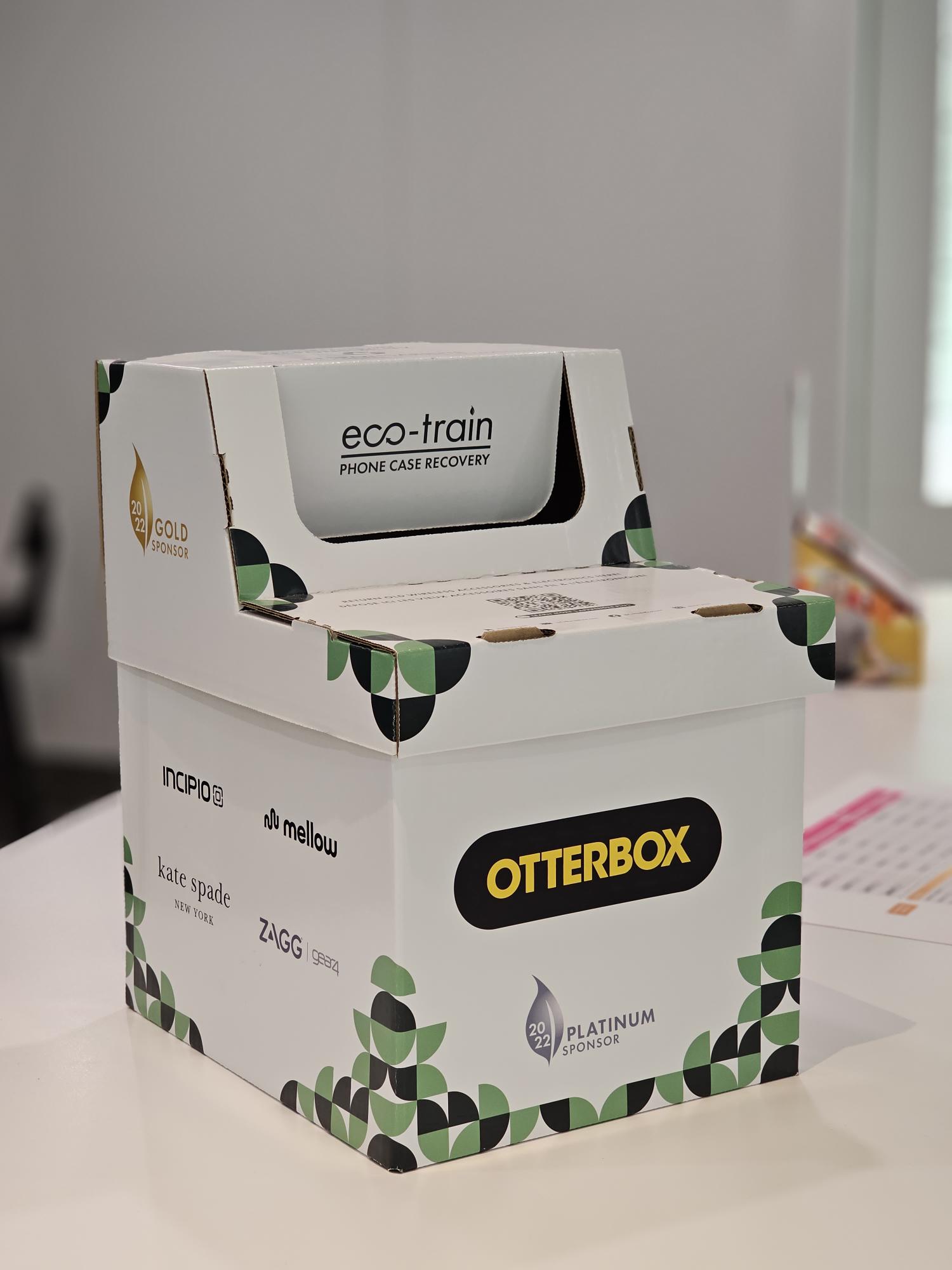 Eco-train phone case recovery box on a counter with sponsor logos including OtterBox, Incipio, kate spade new york, and ZAGG