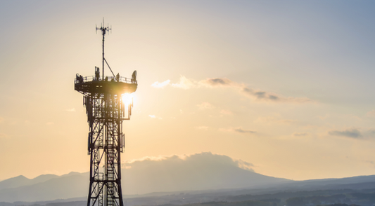 A telecommunications tower backlit by a sunset with mountains in the background | Jump.ca